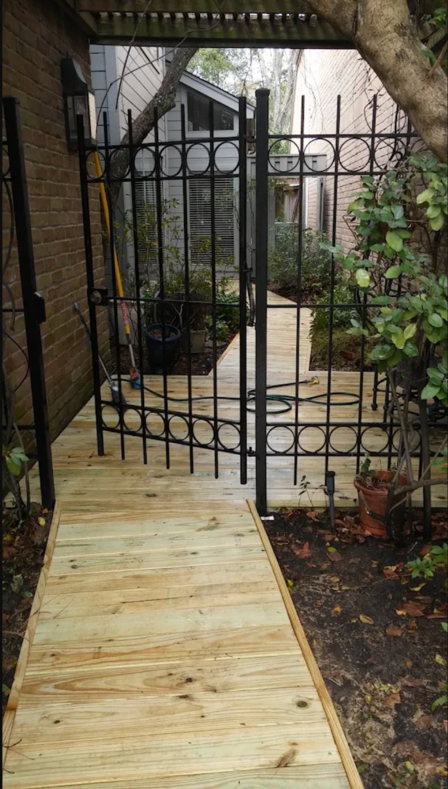 Wooden pathway leading through black metal garden archway in courtyard