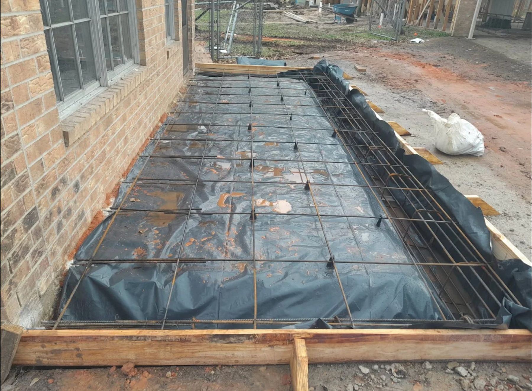 Concrete foundation preparation with reinforcement steel mesh and plastic vapor barrier next to brick building