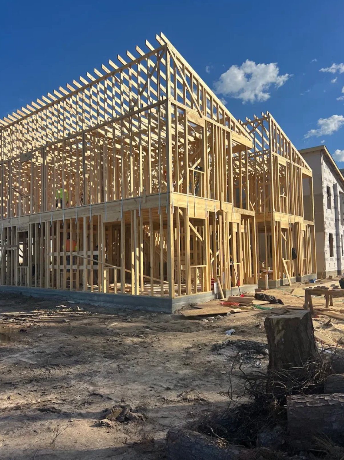 New residential framing under construction with exposed wood studs and roof trusses against blue sky