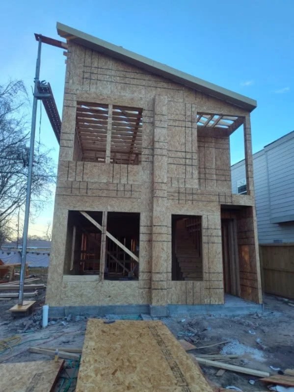 Two-story residential construction with concrete block exterior and wooden window frames under clear blue sky