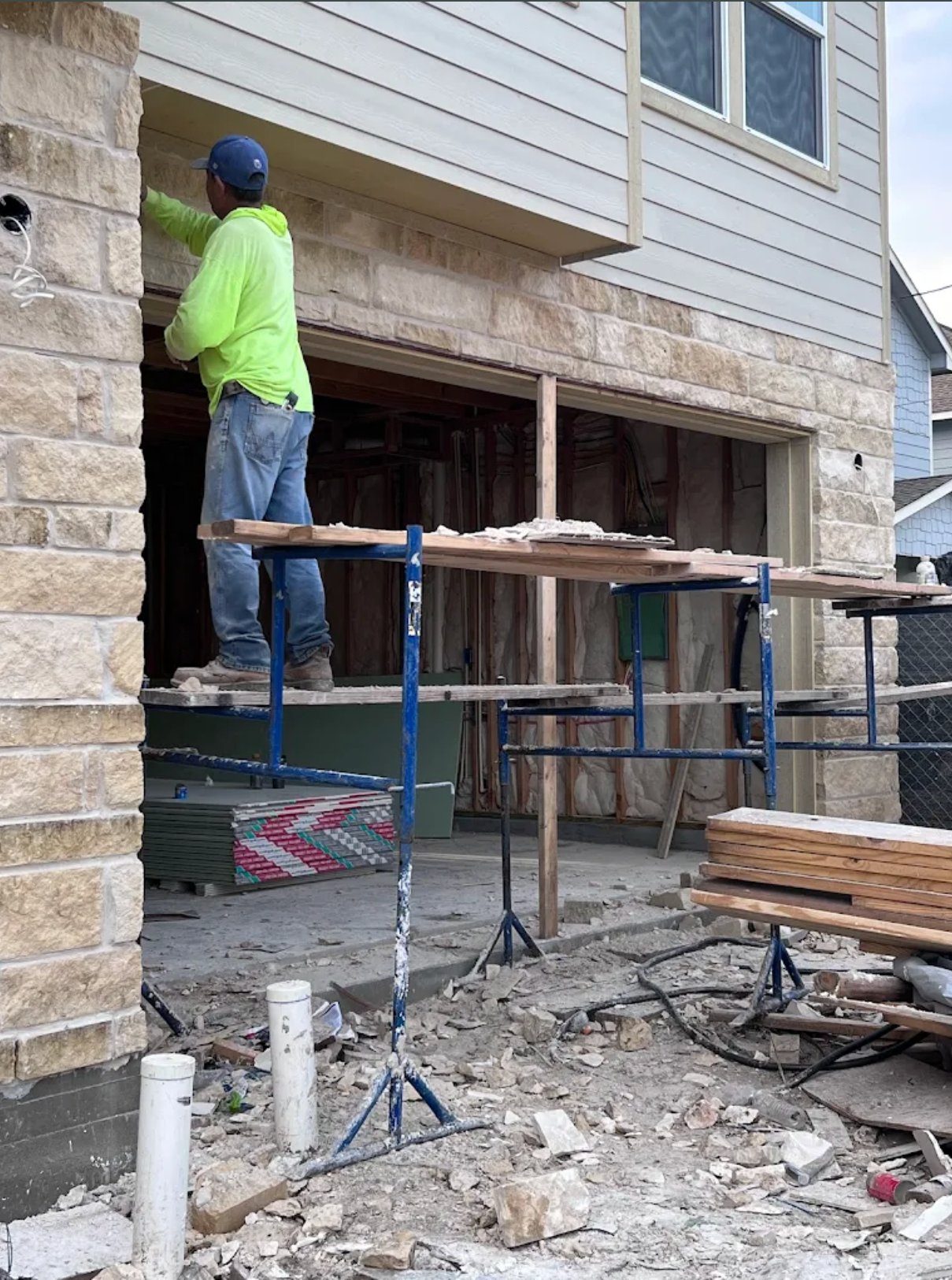 Construction worker in neon yellow shirt and blue hard hat on scaffolding during home renovation