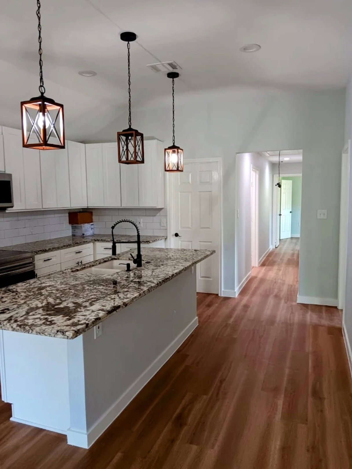 Modern kitchen with white cabinetry, granite countertops, pendant lights, and hardwood flooring