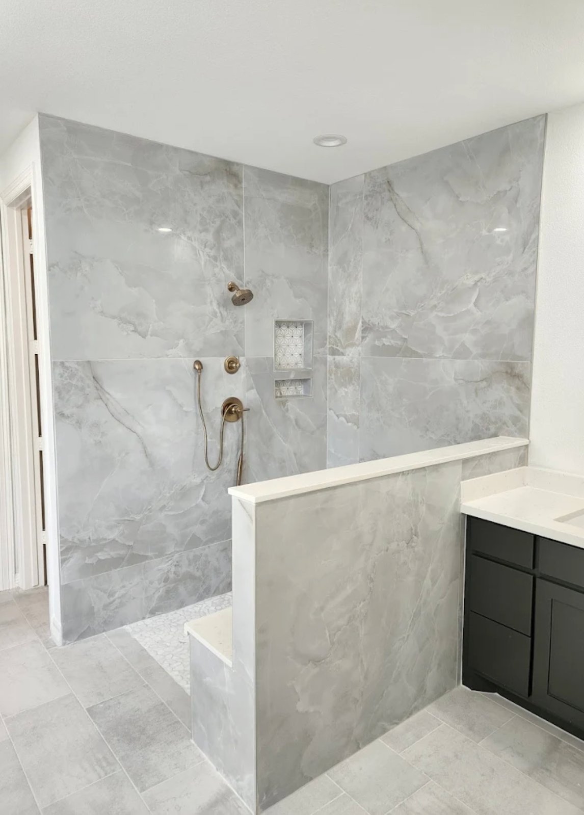 Modern bathroom with marble walk-in shower, bronze fixtures, and dark vanity cabinet