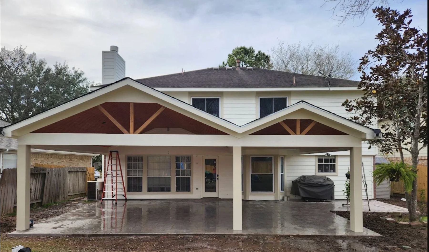 Two-car patio cover with decorative trusses attached to white brick home