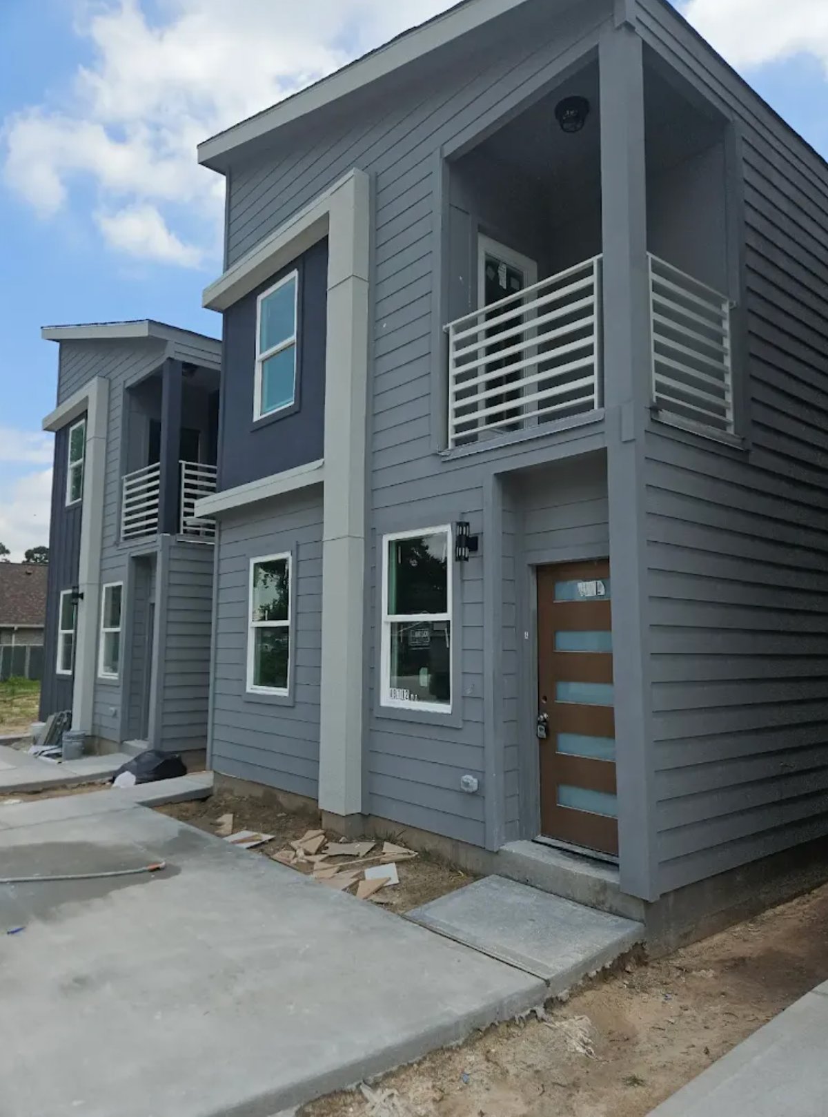 Modern gray two-story house with horizontal siding, metal railings, and wood front door