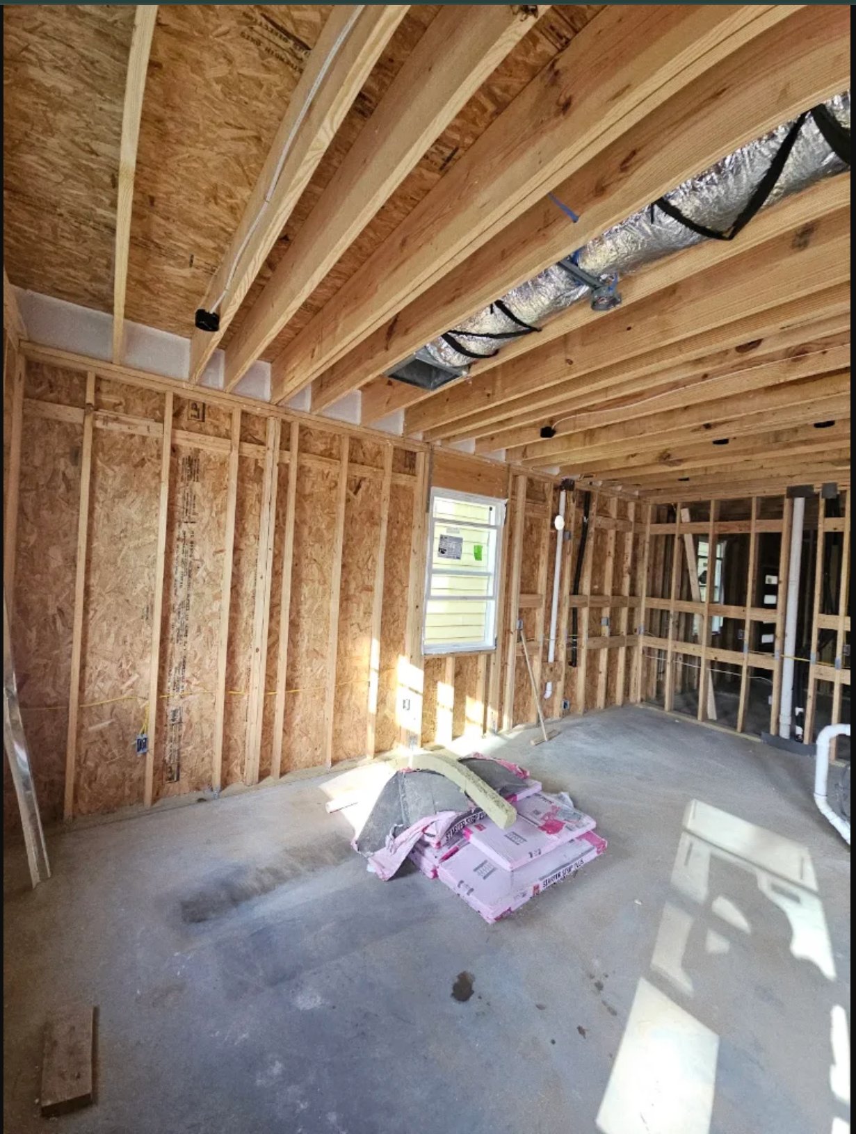 Interior framing of new home construction showing wooden studs, joists, and insulated ductwork