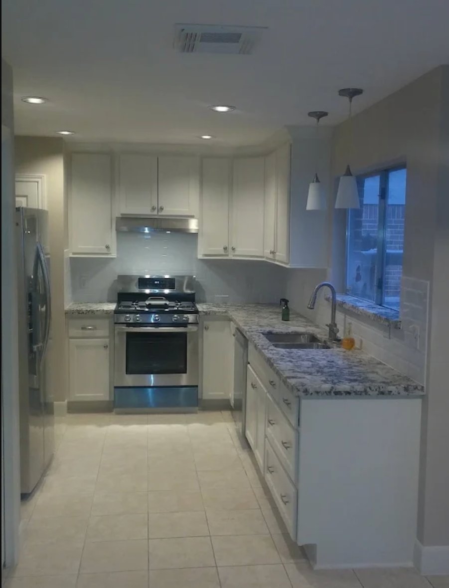 Modern white kitchen with granite countertops, stainless steel appliances, and pendant lighting