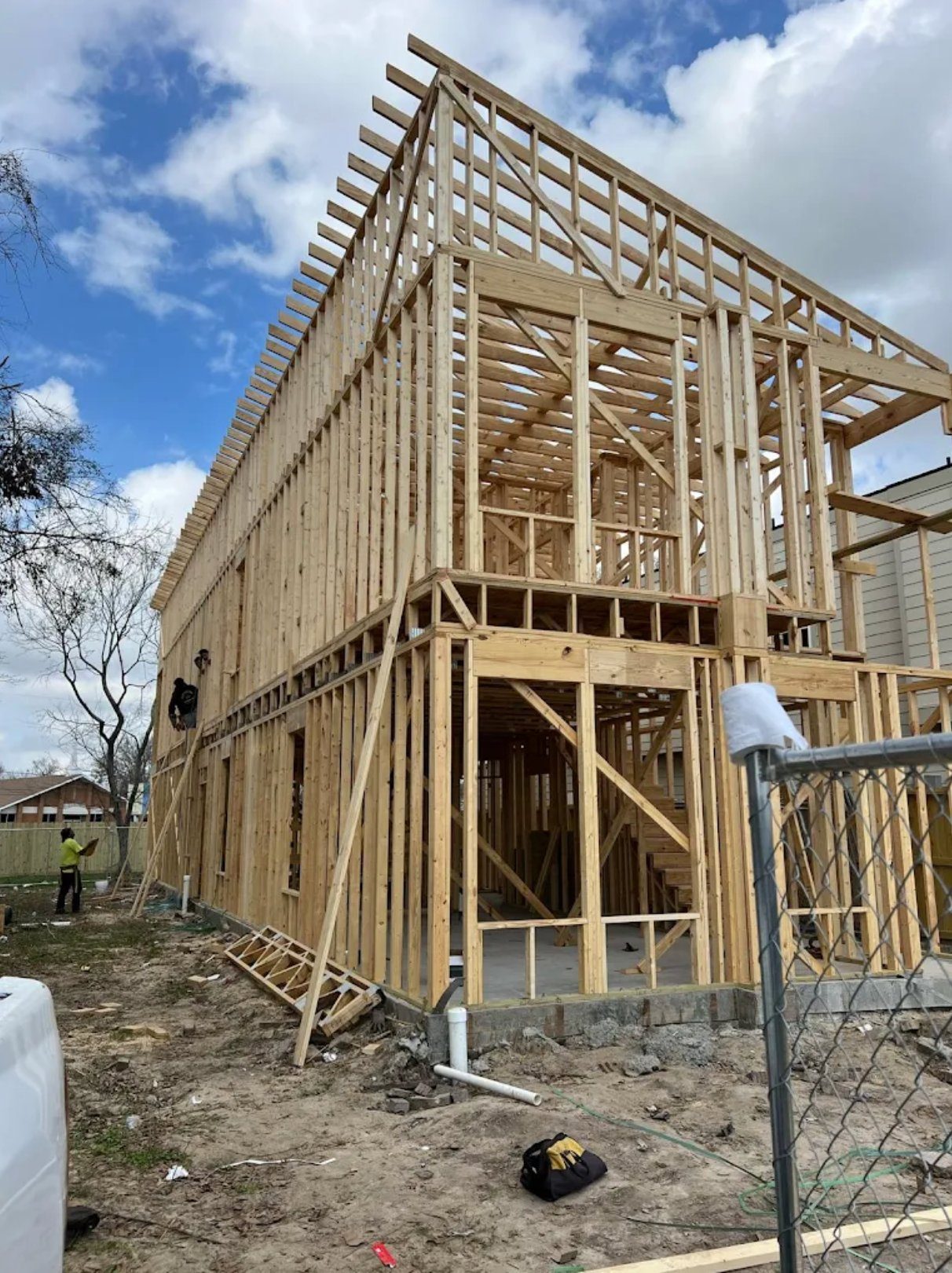 New wooden house frame construction with exposed studs and roof trusses under blue sky